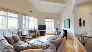 A spacious living room with a fireplace, a flat-screen TV, and a dining area with a table and chairs. - 1BR + Loft | Glacier Lodge | King Bed | Near Gondola | Private Balcony | Free Ski Valet (Whistler)