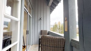 A balcony with a wicker chair, a view of trees, and a wooden post with a thermometer. - 1BR + Loft | Glacier Lodge | King Bed | Near Gondola | Private Balcony | Free Ski Valet (Whistler)