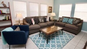 A living room with a sectional sofa, a blue armchair, a coffee table, and patterned rugs. - Perfect vacation Gated Resort with Private Pool (Kissimmee)