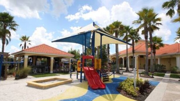 A playground with a red slide and a blue and yellow play area, surrounded by palm trees and buildings with red roofs. - Perfect vacation Gated Resort with Private Pool (Kissimmee)