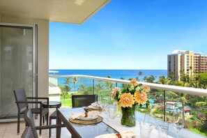 A balcony with a table set for dining, overlooking a pool and ocean view.