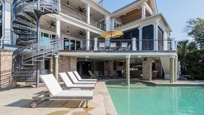 Une maison à deux étages dotée d’une piscine, d’un espace salon extérieur et d’un escalier en colimaçon.