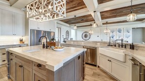Une cuisine spacieuse dotée d’un grand îlot central, d’appareils électroménagers en acier inoxydable et de meubles de rangement en bois.