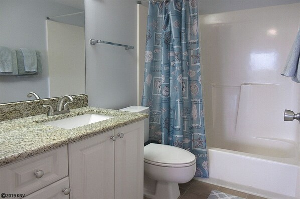 A bathroom with a granite countertop sink, a white toilet, and a bathtub with a blue shower curtain.