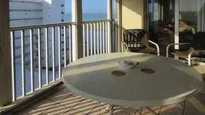 Un balcón con mesa y sillas, vista al mar y un edificio de fondo.