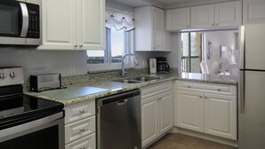 Una cocina con armarios blancos, lavavajillas de acero inoxidable, microondas, estufa y pileta.