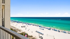Une vue sur la plage depuis un balcon, avec un ciel dégagé, une plage de sable et quelques parasols.