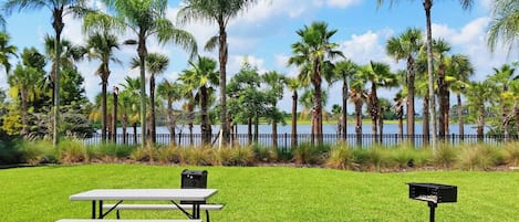 A picnic table and mailbox in a grassy area with palm trees and a fence in the background.