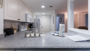 A modern kitchen with white cabinetry, a granite countertop, and a built-in oven. There is a sink with a faucet, a coffee maker, and a toaster. A large window provides natural light.