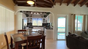 A dining area with a table and chairs, a kitchen with white cabinets and a window, and a living area with a couch and a door leading outside.
