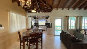 A spacious living area with a dining table and chairs, a sofa, and a kitchen in the background.