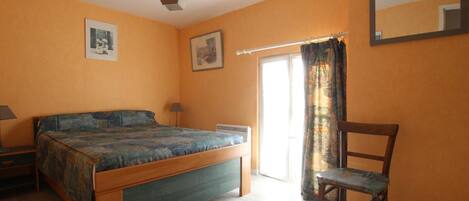 A bedroom with a bed, a chair, a desk, a lamp, a window with curtains, and a ceiling light.