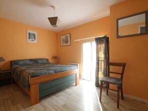 A bedroom with a bed, a chair, a desk, a lamp, a window with curtains, and a ceiling light.