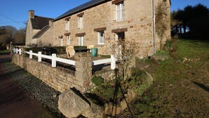 Un bâtiment en pierre avec un toit en pente, une clôture blanche et un espace barbecue à l’extérieur.