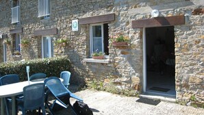Un bâtiment en pierre, à l’aspect rustique, doté d’un espace extérieur aménagé pour s’asseoir et d’une porte donnant accès à l’intérieur.