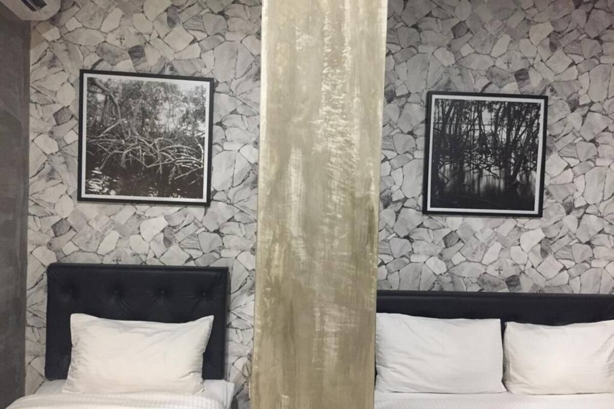 A hotel room with two beds, a stone-patterned wall, and two framed black-and-white forest photographs.