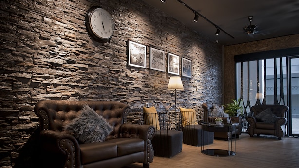 Un salon avec un mur en pierre, une grande horloge et des tableaux encadrés.