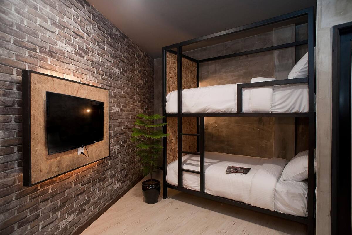 A room with a brick wall, a mounted TV, bunk beds, and a potted plant.
