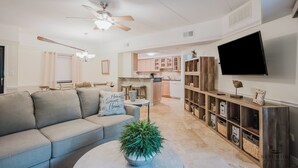 A modern living room with a sectional sofa, a coffee table with a plant, a ceiling fan, and a kitchen in the background. - 123 Forest Beach Villas (Hilton Head Island)