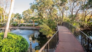 A wooden boardwalk over a body of water, surrounded by lush greenery and trees. - 123 Forest Beach Villas (Hilton Head Island)