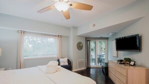 A hotel room with a bed, a ceiling fan, a TV, a desk, and a view of the outside balcony. - 123 Forest Beach Villas (Hilton Head Island)