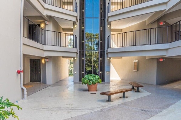 A multi-level atrium with a central glass elevator shaft, potted plants, and benches.