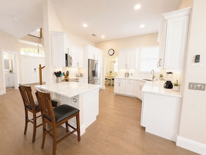 A modern kitchen with white cabinetry, a central island, and a dining area with wooden chairs.