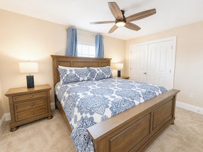 A bedroom with a wooden bed, two bedside tables, a ceiling fan, and a door.