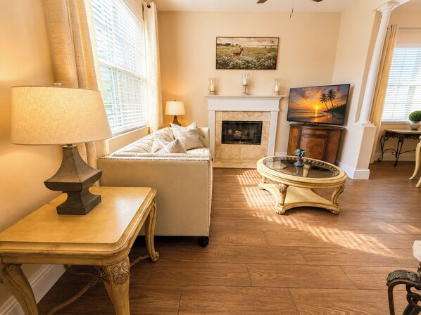 A living room with a sofa, a table with a lamp, a fireplace, and a television.