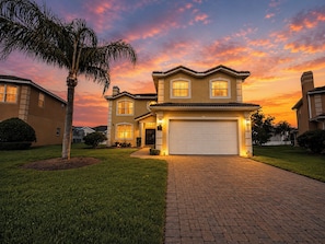 A two-story house with a garage, surrounded by well-maintained lawns and a palm tree.