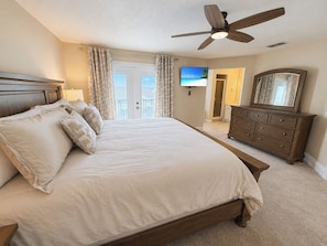 A bedroom with a bed, a dresser, a ceiling fan, and a television.
