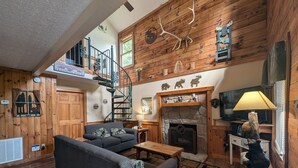 A cozy living room with a fireplace, a staircase, and rustic wooden walls. - ER13 - Moose Manor  Great location - Close to town! (Pigeon Forge)