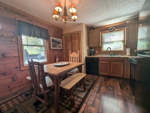 A wooden cabin interior with a dining table, chairs, a bench, a chandelier, wooden cabinets, a dishwasher, and a refrigerator. - ER13 - Moose Manor  Great location - Close to town! (Pigeon Forge)
