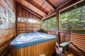 Una cabaña de madera con un jacuzzi, un banco y una ventana con vistas a un bosque.