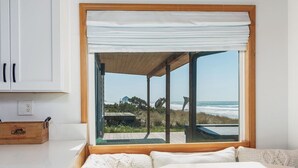 Una habitació amb una finestra gran que dona a l'oceà, una banca de fusta i un llit blanc.