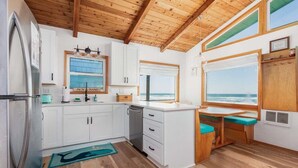 Una cuina compacta amb armaris blancs, un rentaplats integrat i vista a l'oceà a través de grans finestres.