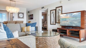 A living room with a sofa, a glass coffee table, a TV, and framed artwork on the wall. - 🌊 Islander #506 – Affordable Gulf-View Getaway! 🌴✨ (Destin)