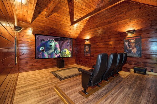 Una habitación con paneles de madera, un televisor de pantalla plana grande, sillas de cuero negro y un cartel en la pared.