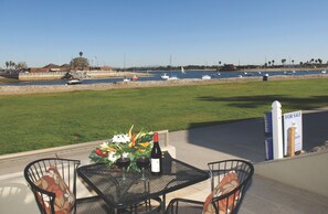 Un patio con una mesa lista para dos personas, con vista a un puerto deportivo con barcos y un cielo despejado.