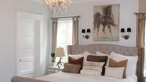 A bedroom with a large bed, a bench, a chandelier, and a painting on the wall.