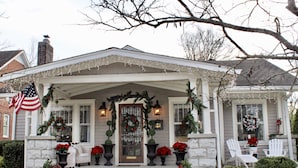 A house with a porch decorated with Christmas lights, wreaths, and poinsettias.