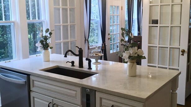A kitchen with a large island, white cabinetry, a double sink, and pendant lighting.