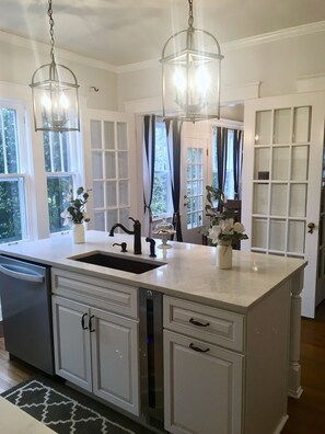A kitchen with a large island, white cabinetry, a double sink, and pendant lighting.