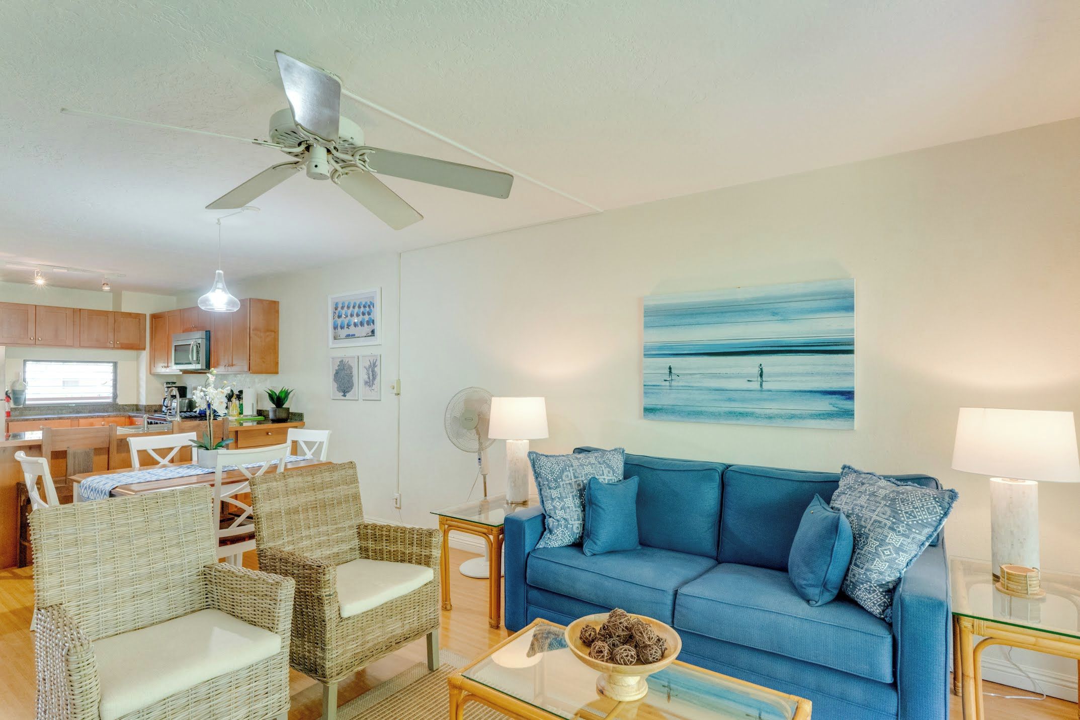Ein Wohnzimmer mit blauem Sofa, Korbstühlen, einem Glastisch und Deckenventilator.