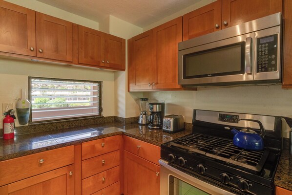 A kitchen with wooden cabinets, a stainless steel microwave, a gas stove, and a window with blinds.
