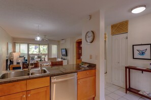 A kitchen with a dishwasher, a sink, and a granite countertop. There is a clock on the wall and a framed picture above the sink.