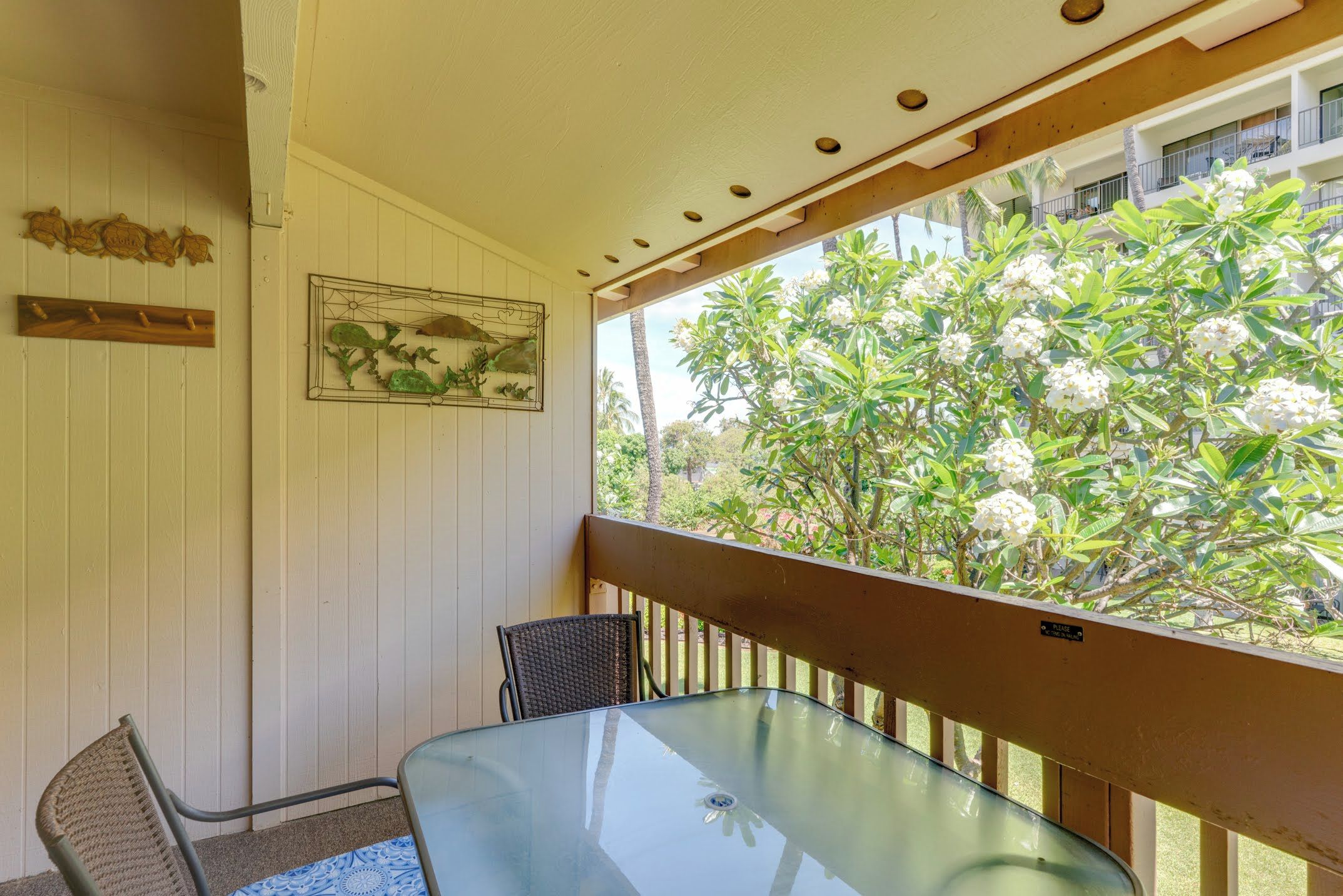A glass table and chair set on a balcony with a view of a tree with white flowers.