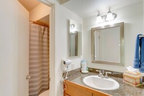 A bathroom with a white sink, a mirror, a towel rack with a blue towel, and a shower curtain.