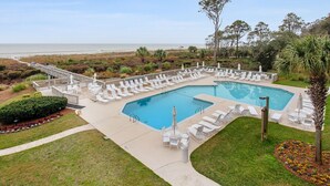 A pool area with multiple lounge chairs and a small bridge leading to the beach.