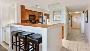 A modern kitchen with a central island, bar stools, wooden cabinets, and stainless steel appliances.